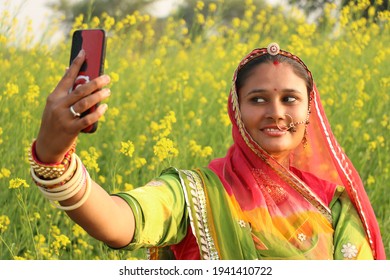 beautiful Rajasthani (Rajput) woman takes selfie from mobile in mustard field. Rajasthani lady takes her selfie. 