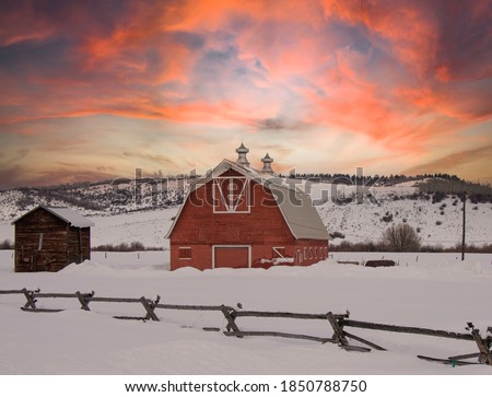 Beautiful red barn in rural Wyoming surrounded by snow as a gorgeous sunset colors the landscape hints or orange, red, and purple during winter, no people