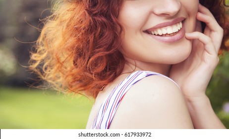 Beautiful Red Haired Woman With Fresh Flawless Skin And Curly Hairstyle In Dress, Smiling Cheerfully In Park. Ideal Teeth. Sunny Day. Close Up Of A Smile