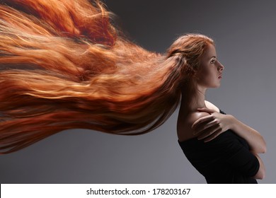 Beautiful Red Headed Woman With Long Hair Flying Against Gray Background, Side View