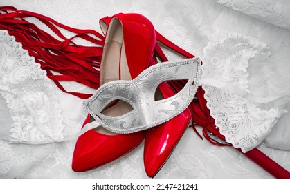 beautiful red stilettos and a whip, white mask and stockings on an openwork white fabric background