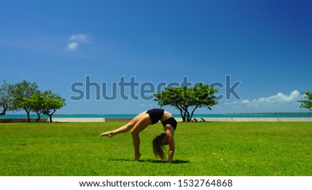 beautiful red-haired curly girl model on green grass do yoga. beautiful blonde on a green lawn performs acrobatic elements. flexible gymnast in black do handstand in split
