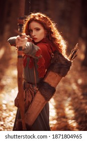 Beautiful red-haired girl archer of the Middle Ages stands in a forest. Fantasy world.