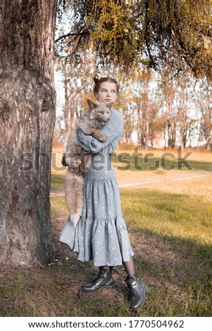 Beautiful red-haired girl with a fox in her arms against the background of the forest, animal rescue, domestication of wildlife, a woman with an original hairstyle