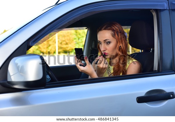 Beautiful\
red-haired woman makes up lips in the\
car