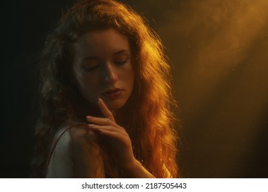 Beautiful Redhead Freckled Woman With Long Curly Hair Posing In Darkness, Smoke And Warm Light. Art Studio Portrait. Copy, Empty Space For Text 