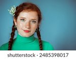 Beautiful redhead freckled woman wearing green turtleneck with bouquet of lily of the valley flowers, posing on blue background. Close up studio portrait. Copy, empty, blank space for text
