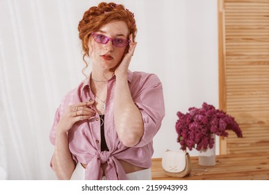 Beautiful redhead freckled woman wearing trendy lilac color glasses, silk shirt with knot, many rings, necklace. Copy, empty space for text