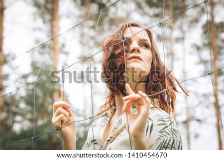 Beautiful redhead girl behind fence outdoors. Psychological concept of limiting beliefs, phobias and fears