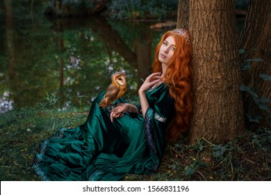 Beautiful redhead girl in green dress with owl near the lake