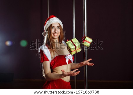 Beautiful redhead strip-tease girl in a dress and Santa hat is standing near pylon catching falling presents, looking at camera and smiling, isolated on white background..