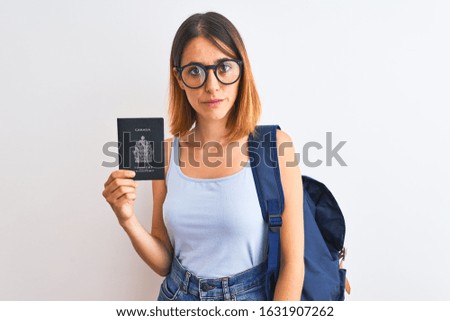 Beautiful redhead student woman wearing backpack and holding passport of canada with a confident expression on smart face thinking serious