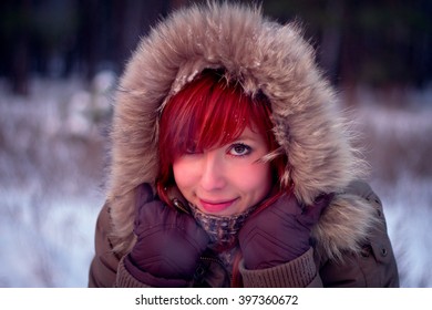 The Beautiful Redhead Woman Hides Her Face In The Hood With Fur From Winter Wind.
She Warming In The Hood From The Cold. Her Hands In Gloves.
Her Cheeks Rosy From The Cold.
Portrait Of A Cute Woman.
