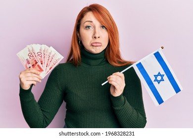 Beautiful Redhead Woman Holding 20 Shekels Banknotes And Israel Flag Depressed And Worry For Distress, Crying Angry And Afraid. Sad Expression. 