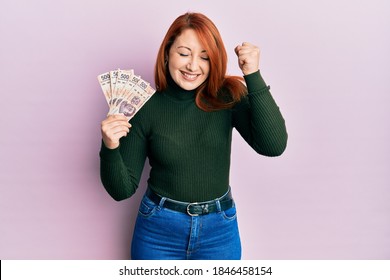 Beautiful redhead woman holding 500 mexican pesos banknotes screaming proud, celebrating victory and success very excited with raised arm 