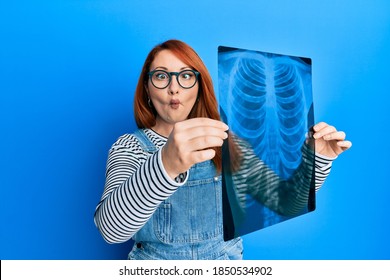 Beautiful Redhead Woman Holding Chest Radiography Making Fish Face With Mouth And Squinting Eyes, Crazy And Comical. 