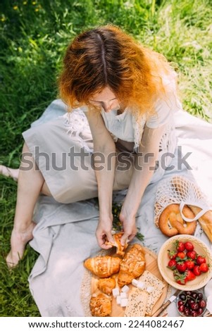 Beautiful redhead woman on picnic. She smiles, eat strawberrie and enjoys summer