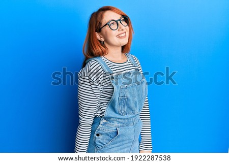 Beautiful redhead woman wearing casual clothes and glasses looking to side, relax profile pose with natural face and confident smile. 