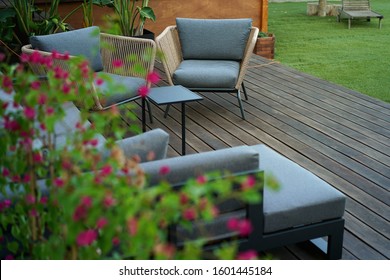 Beautiful relaxing spot in the garden with comfortable chairs and sofa standing on a wooden deck terrace near the green grass                              