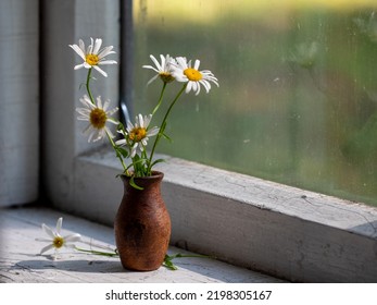 Beautiful Retro Still Life With Chamomile Flowers In Clay Jug On Windowsill Of Old Window Of Old Country House, Summer Cottage. Close Up, Copy Space. Floral Home Decoration. Country Life Concept