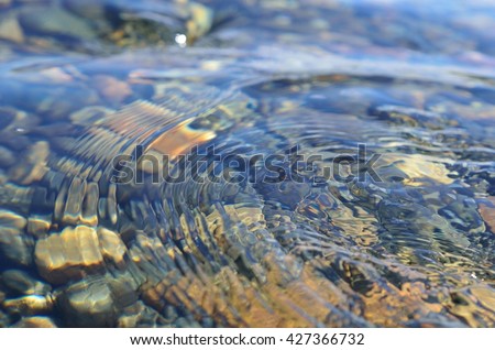 beautiful ripples on river flow over colorful stones in summer sunshine