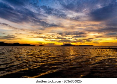 Beautiful River Shoreline Where The Sun Sets In The Sunset With Golden Yellow Clouds. Beautiful Scenery Before The End Of The Day