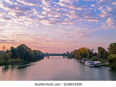 Beautiful river at sunset. Railway bridge over the river in the distance.  Trees and boats on the riverbank. - Shutterstock ID 1628651830