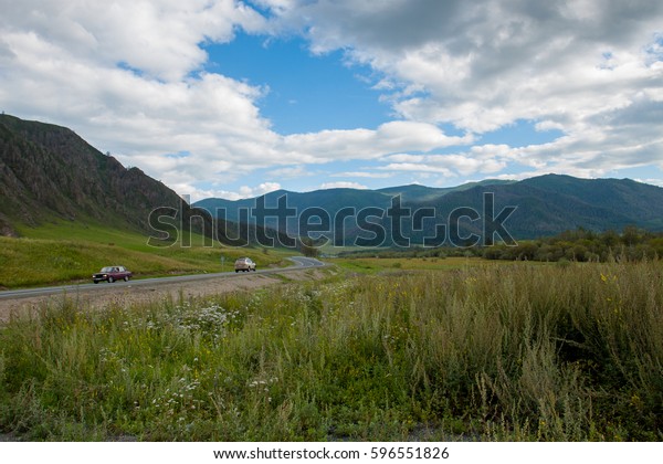 Beautiful road in the mountains. Mountain landscape on\
the Chuyskiy Tract in the Altai mountains. On the road the car\
drives behind a sharp turn, around the beautiful mountains and\
cloudy sky. 