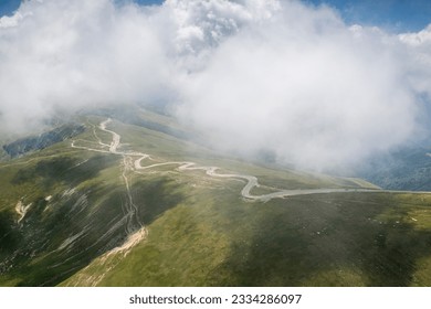 Beautiful roads of Romania. Aerial photo with Transalpina road on top of the mountains with big clouds above. Curved waving road.