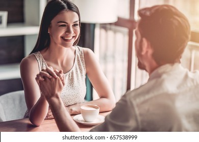 Beautiful romantic couple in cafe is sitting hand to hand, looking on each other and smiling.