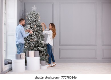 Beautiful romantic couple dressing up a Christmas tree in an interior living room, minimalism or classic, gray walls with stucco, white wooden floor, space                 
    - Powered by Shutterstock