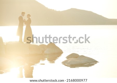 Beautiful romantic couple in elegant black clothing stand thoughtfully and tensely on the seacoast at sunset holding their hands. Love, relationship. Love novel. 19th century style. Copy space.