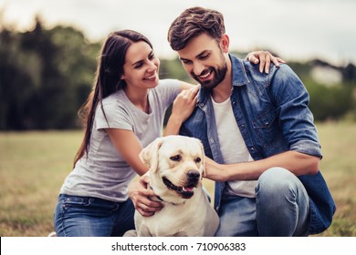 Beautiful Romantic Couple Is Having Fun With Their Dog Labrador Retriever Outdoors.