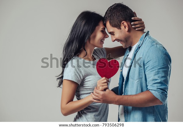 グレイの背景に美しいロマンチックなカップル 魅力的な若い女性とハンサムな男性が赤い心を手に抱きしめている 聖バレンタインデーおめでとう の写真素材 今すぐ編集