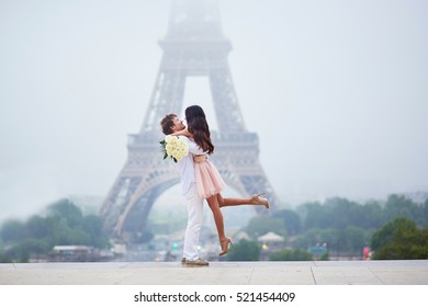 Beautiful romantic couple in love with bunch of white roses having fun near the Eiffel tower on a cloudy and foggy rainy day. Paris, France - Powered by Shutterstock