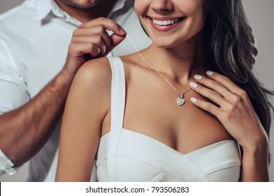 Beautiful romantic couple in love isolated on grey background. Handsome man is wearing necklace on his attractive young woman. Happy Saint Valentine's Day!