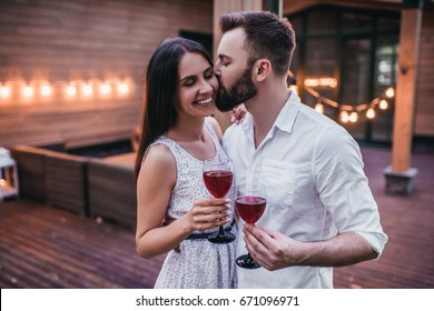 Beautiful romantic couple on house's terrace. Drinking wine, hugging, smiling and enjoing the company of each other. - Powered by Shutterstock