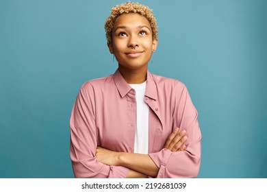 Beautiful romantic female with blond short curly hair in pink silk shirt standing with inspired face expression looking up with dreamy look and crossed hands, recollecting best memories - Shutterstock ID 2192681039