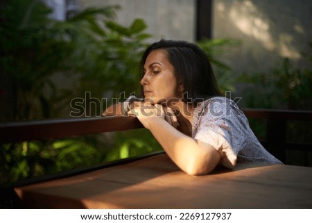 Beautiful romantic middle-aged black hair woman in pink dress sitting on table, grieving alone, missing by someone in summer cafe in morning time