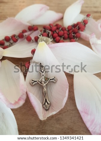 Beautiful rosary with cruzifix of Christ laying softly on tulip petals on wodden vintage table - for comunion/church/hope concepts