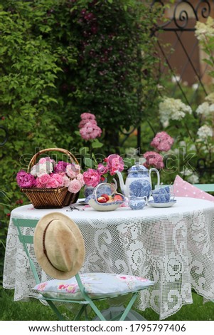Beautiful roses in wicker basket, porcelain  tea set, fruit on knitted tablecloth, Lovely scene in summer garden, Vintage style, outdoors and space, daylight