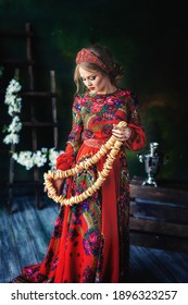 A beautiful Russian girl in a kokoshnik and traditional dress stands and holds a bunch of bagels in her hands. Russian folk, retro, ethno. Pavlovo Posad shawl. Selective focus photo
