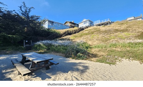 Beautiful rustic elevated beachhouse with personal access to the beach via a wooden staircase and wooden bench. Clear skies. Pacific ocean. 