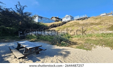 Beautiful rustic elevated beachhouse with personal access to the beach via a wooden staircase and wooden bench. Clear skies. Pacific ocean. 