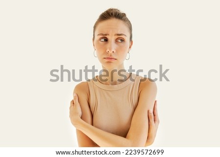 Beautiful sad girl hugging herself, giving herself support and protection, feeling lonely and depressed, looking aside with thoughtful upset facial expression, ready to burst into tears. Body language