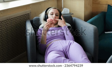 Beautiful sad girl spends time alone at home. The girl listens to music in headphones and eats sweet cakes.