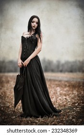 A beautiful sad goth girl holds black umbrella. Grunge texture effect 