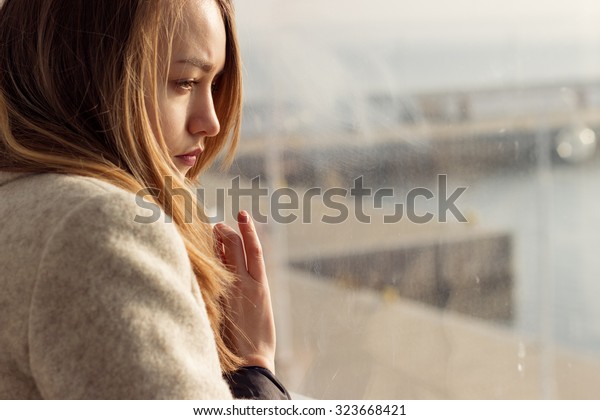 窓の近くに座っている美しい寂しい女の子が行方不明です の写真素材 今すぐ編集