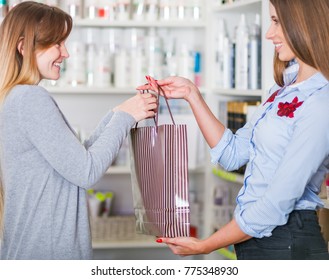 Beautiful Saleswoman At Beauty Store Giving Shopping Bag Full Of Cosmetics To Customer