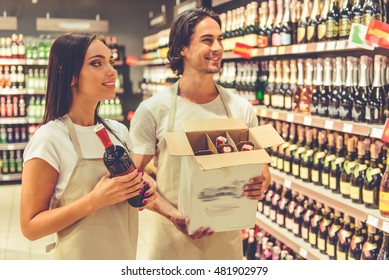 Beautiful saleswoman and salesman in aprons are smiling while arranging bottles of beverage in the supermarket - Powered by Shutterstock